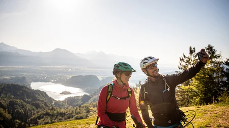 Zwei Fahrradfahrer machen Selfie mit Berg- und Seeblick im Hintergrund
