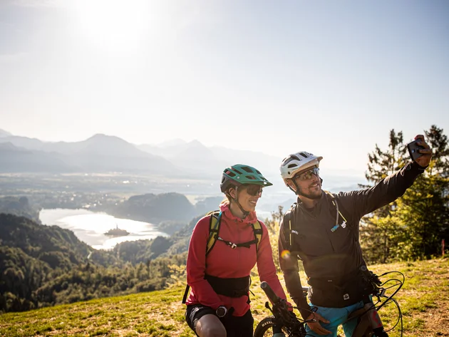 Zwei Fahrradfahrer machen Selfie mit Berg- und Seeblick im Hintergrund