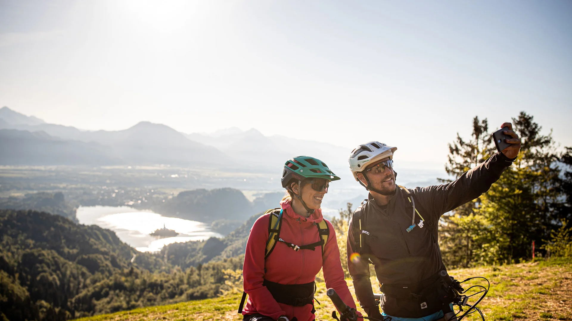 MTB-Bucket List für Slowenien © Bled - Samo Vidic Zwei Fahrradfahrer machen Selfie mit Berg- und Seeblick im Hintergrund