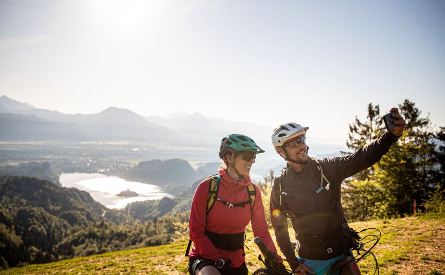 Two cyclists taking a selfie with mountain and lake view in background