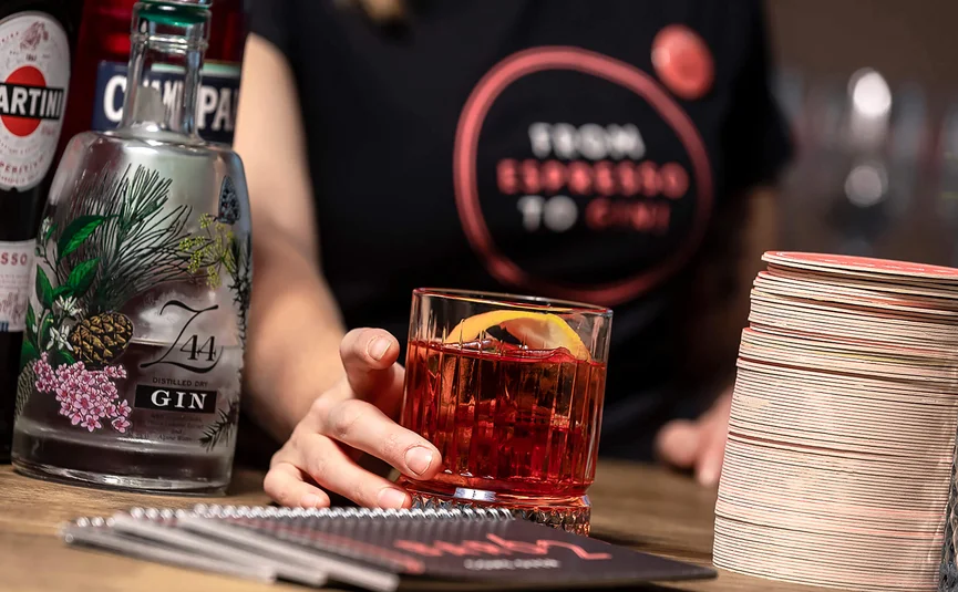 Hand holding glass of red cocktail with lemon slice next to gin bottle