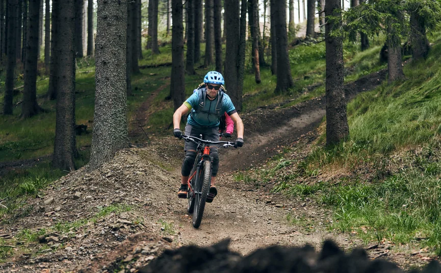 Man wearing blue helmet mountain biking on forest trail