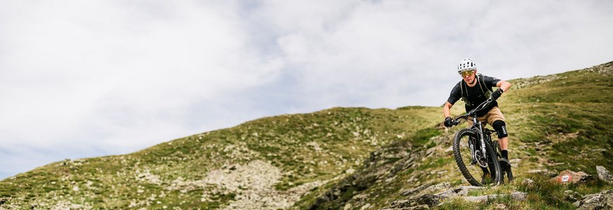 Mountainbiker fährt auf felsigem Bergpfad bei bewölktem Himmel