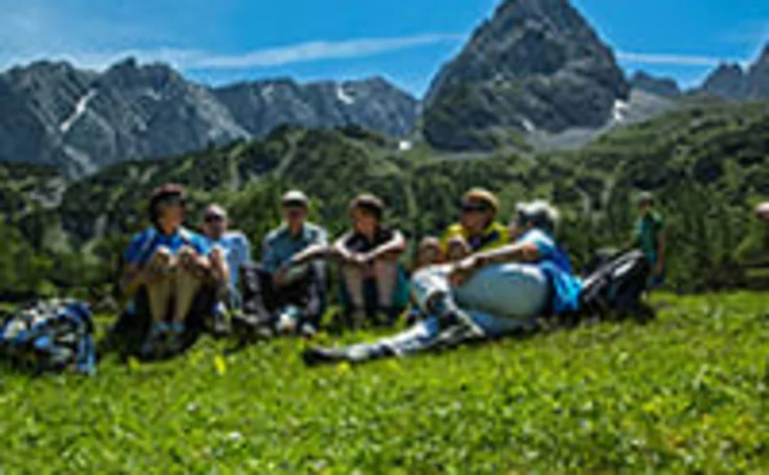 Group of hikers resting on green meadow with mountain backdrop