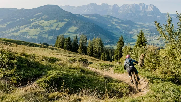 Mountainbiker fährt auf bergigem Pfad mit Blick auf bewaldete Hügel und Berge