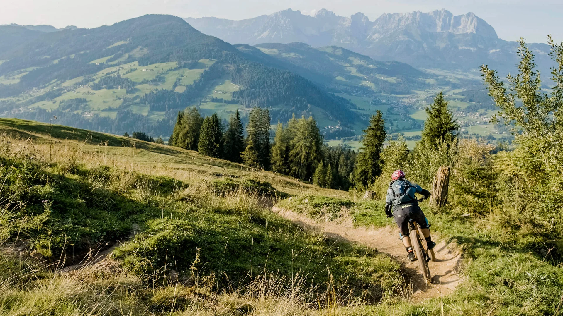 Mountainbiker fährt auf bergigem Pfad mit Blick auf bewaldete Hügel und Berge