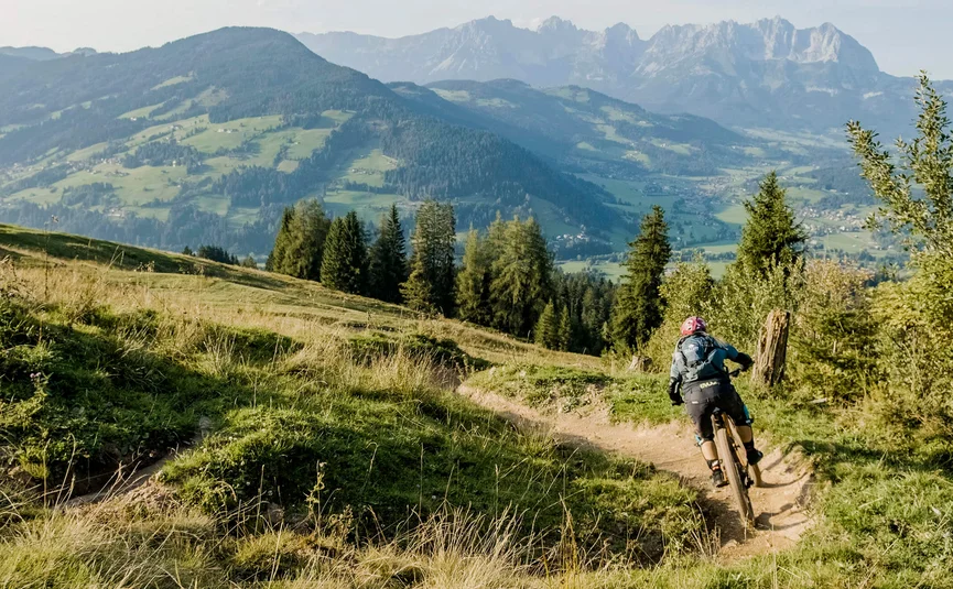 Mountain biker rides on a rocky trail with forested hills and mountains in the background