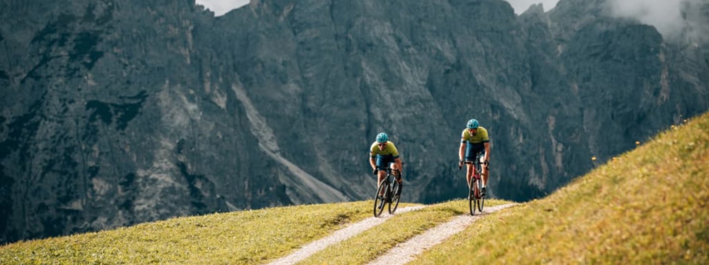Two cyclists riding on a mountain trail with rocky cliffs in the background