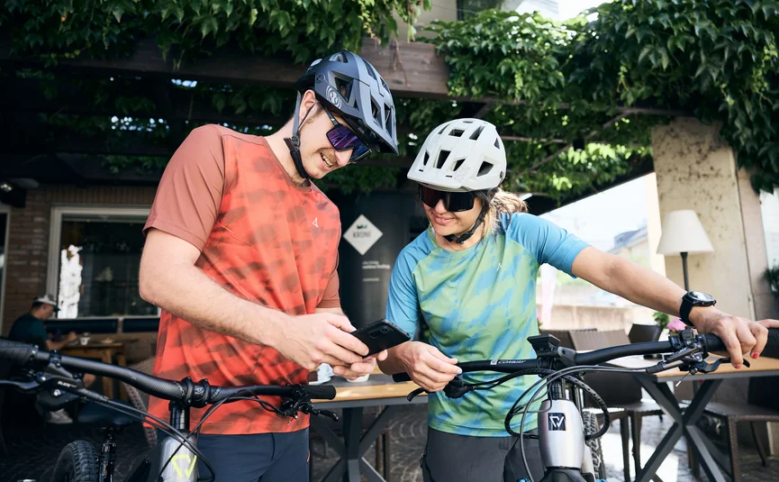 Zwei Radfahrer schauen auf ein Smartphone vor einem Café