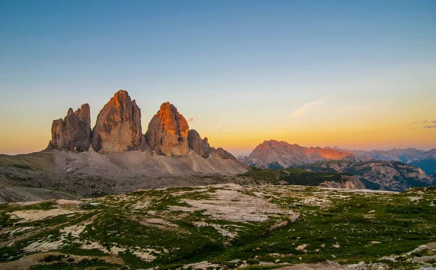 Drei Zinnen im Sonnenuntergang mit grüner Bergwiese im Vordergrund