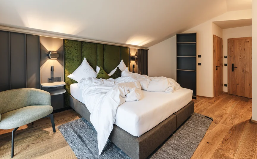 Unordentliches Bett mit grüner Kopfteil in modernem Schlafzimmer mit Holzfußboden