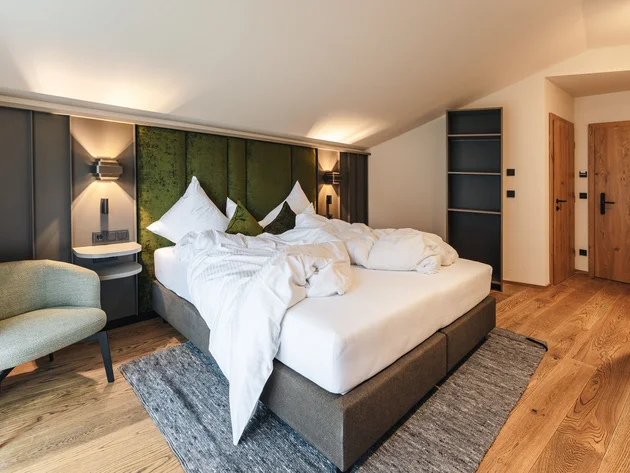 Unordentliches Bett mit grüner Kopfteil in modernem Schlafzimmer mit Holzfußboden