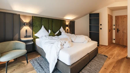Unordentliches Bett mit grüner Kopfteil in modernem Schlafzimmer mit Holzfußboden