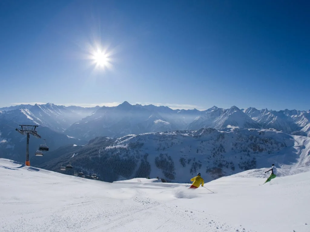 Zonnige dag met skiërs op besneeuwde berghelling en Alpen op de achtergrond