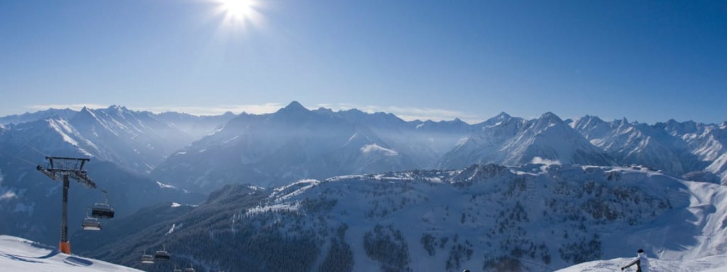 Sun-Skiing Sunny day with skiers on snowy mountain slope and Alps in the background