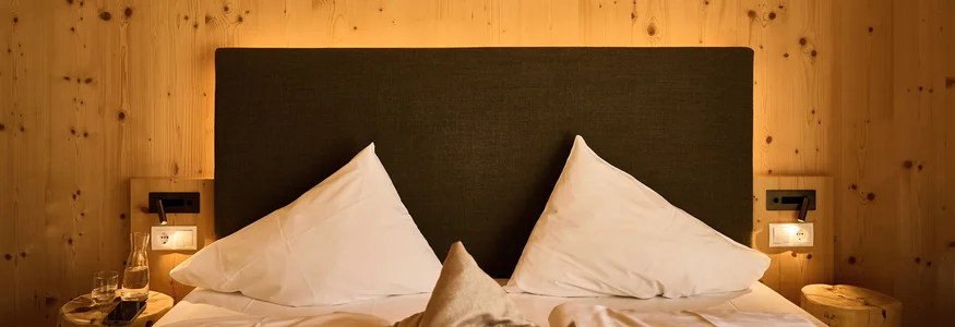 Gemütliches Doppelbett mit weißen Kissen und Holzwand im Hintergrund