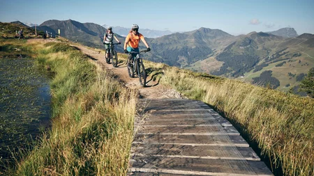 Zwei Mountainbiker fahren auf einem Bergweg mit Alpenblick