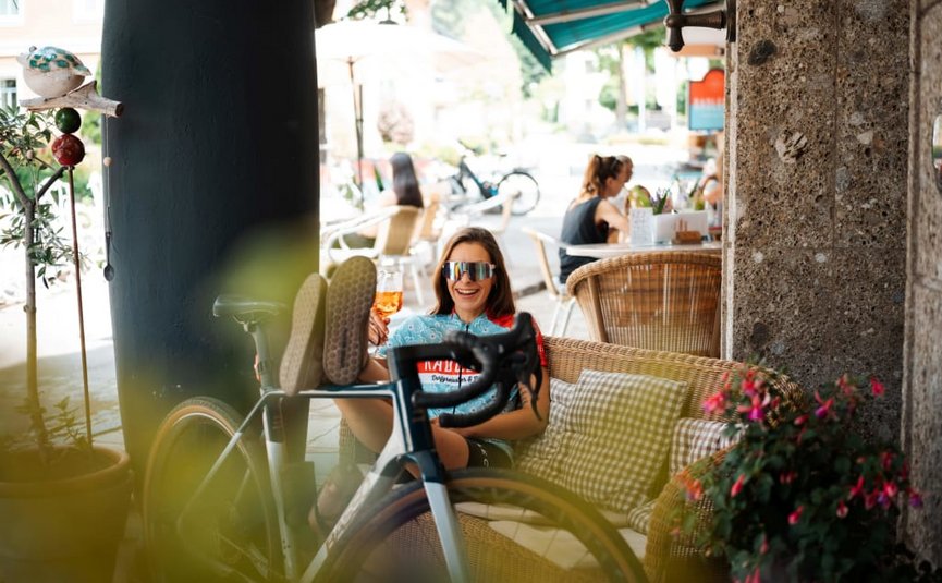 Gravelweekends im Wonnemonat Mai Frau entspannt im Café mit Fahrrad und Getränk an sonnigem Tag