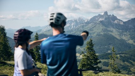 Two cyclists looking at mountain panorama in the Alps on a sunny day