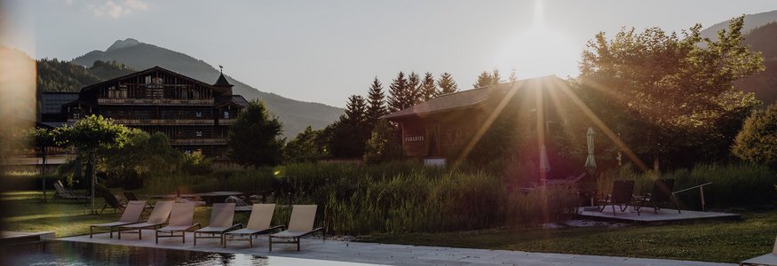 Pool mit Liegestühlen vor Berghotel im Sonnenuntergang