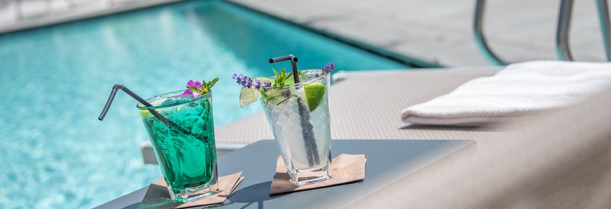 Zwei bunte Cocktails auf einem Beistelltisch neben einem Pool