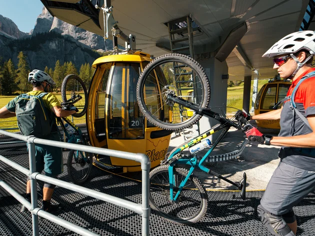 Zwei Radfahrer laden Mountainbikes in gelbe Seilbahn-Gondeln in den Bergen