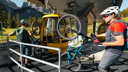 Zwei Radfahrer laden Mountainbikes in gelbe Seilbahn-Gondeln in den Bergen
