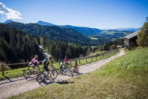 Family riding mountain bikes on a trail with scenic forested hills in the background