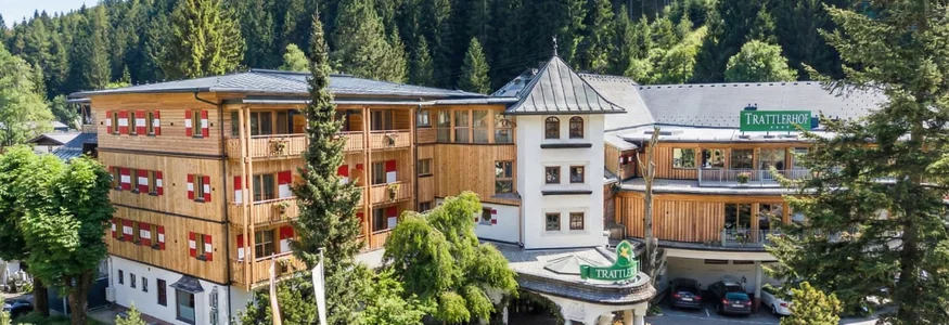 Hotel Trattlerhof umgeben von Bäumen und Bergen im Sommer