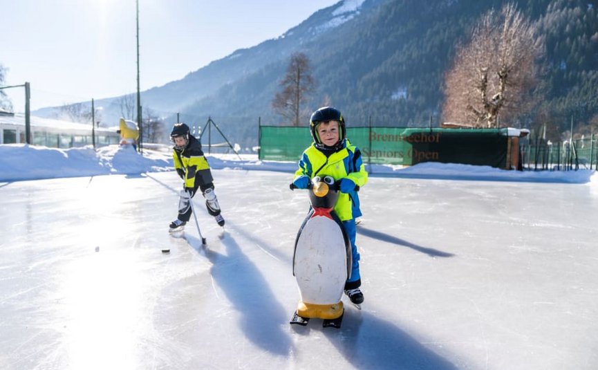 Children ice skating with helmets using a penguin aid on an ice rink