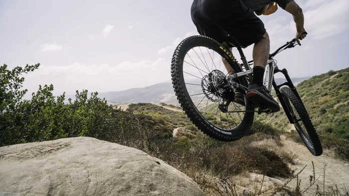 Mountainbiker springt über einen felsigen Trail in hügeliger Landschaft