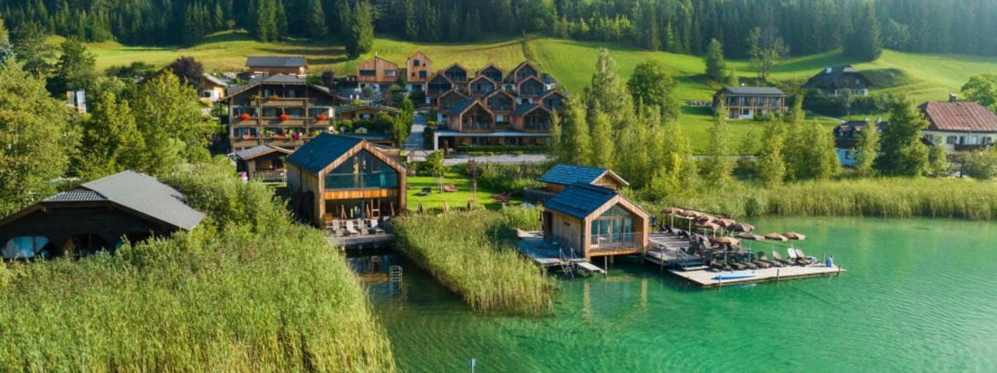 See mit grünen Hütten am Ufer und bewaldeten Bergen im Hintergrund