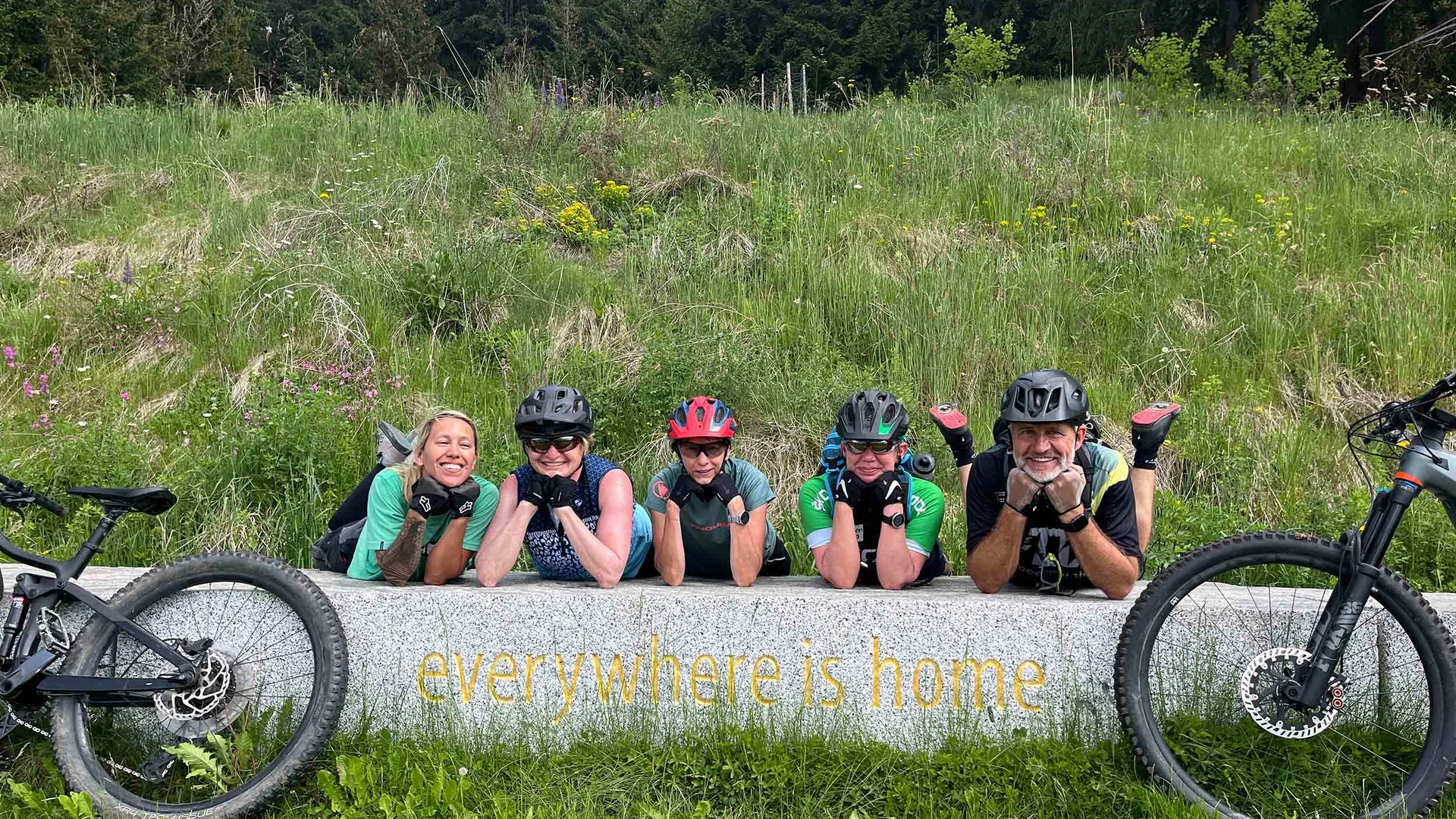 Mountainbike-Saisonstart am Kronplatz © Hotel Innerhofer Fünf Radfahrer lächeln auf einer Bank mit der Aufschrift überall ist Heimat