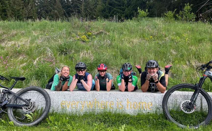 Five cyclists smiling on a bench with the text everywhere is home