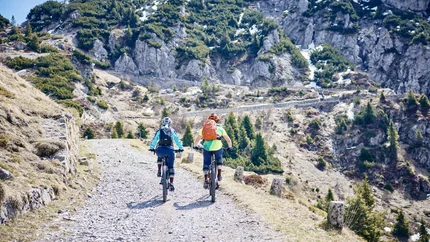 Zwei Radfahrer fahren auf einem Bergweg mit Felsen und Nadelbäumen