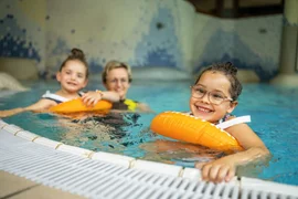 Happy Family week Three children swimming with floaties in an indoor pool