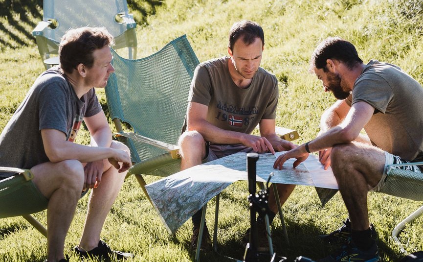 Three men planning a bike route using a map on the grass