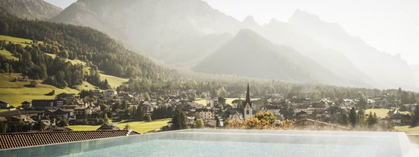 View of a heated infinity pool with mountains and village in the background