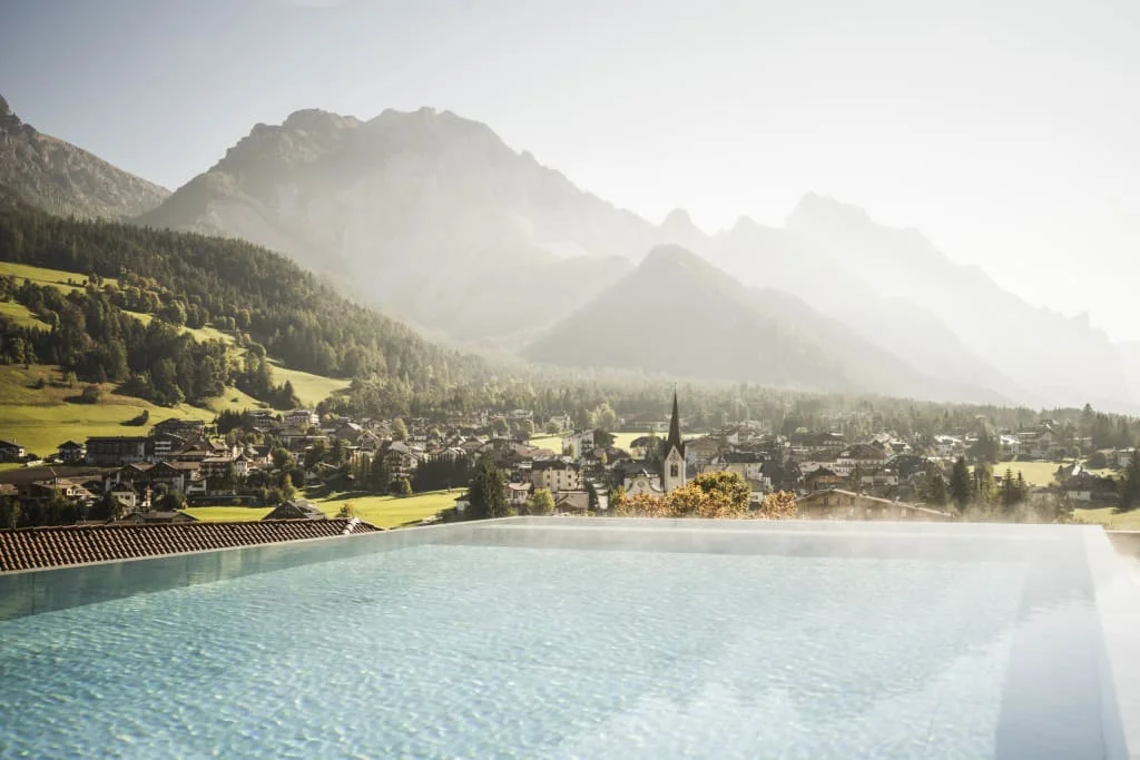 View of a heated infinity pool with mountains and village in the background