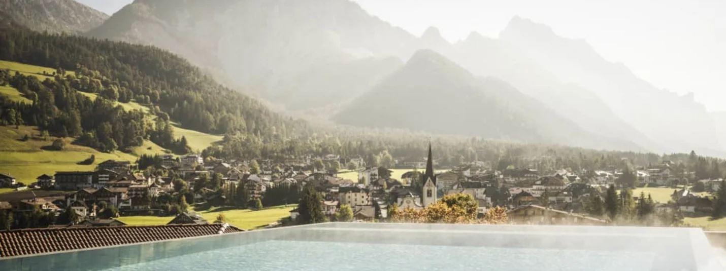 Autumn Special Blick auf ein beheiztes Infinity-Pool mit Berg und Dorf im Hintergrund
