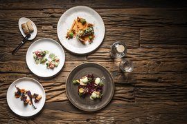 Vier artistiek opgemaakte gourmetgerechten op een rustieke houten tafel