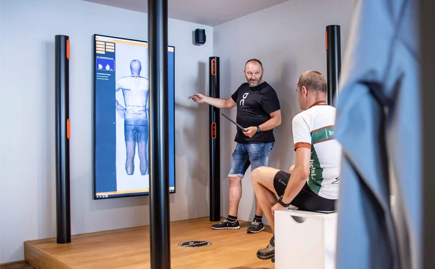 Mann erklärt 3D-Körperanalyse auf Bildschirm in Trainingsraum