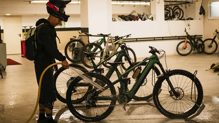Person wäscht Mountainbike in einer Garage mit Wasserschlauch