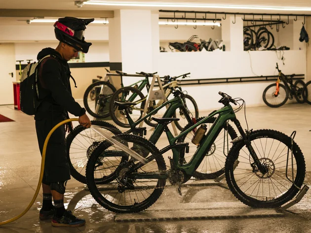 Person wäscht Mountainbike in einer Garage mit Wasserschlauch