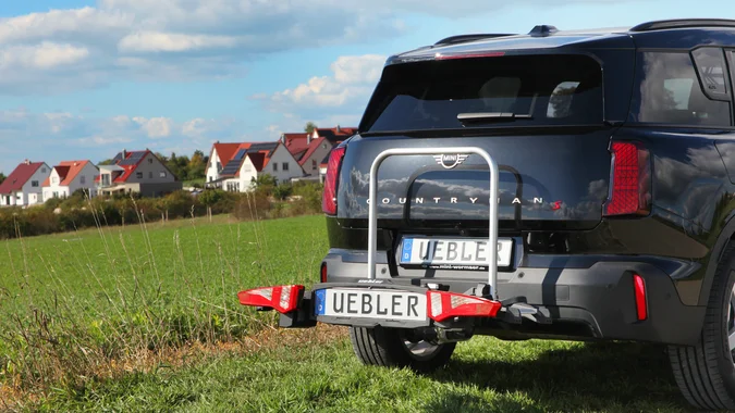 Schwarzer MINI Countryman mit Fahrradträger auf einer Wiese vor Häusern
