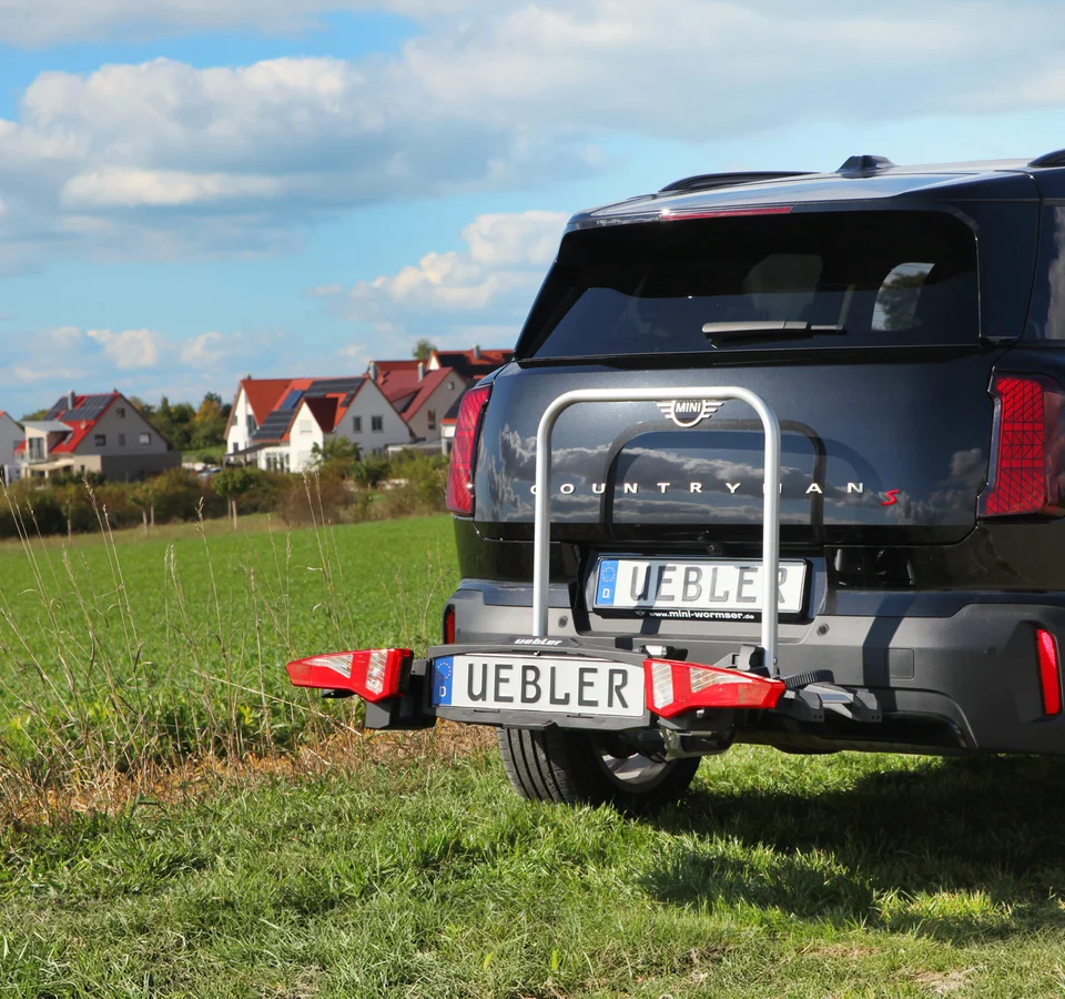 Sicher unterwegs mit dem Testsieger © Karl Pfeifer Schwarzer MINI Countryman mit Fahrradträger auf einer Wiese vor Häusern