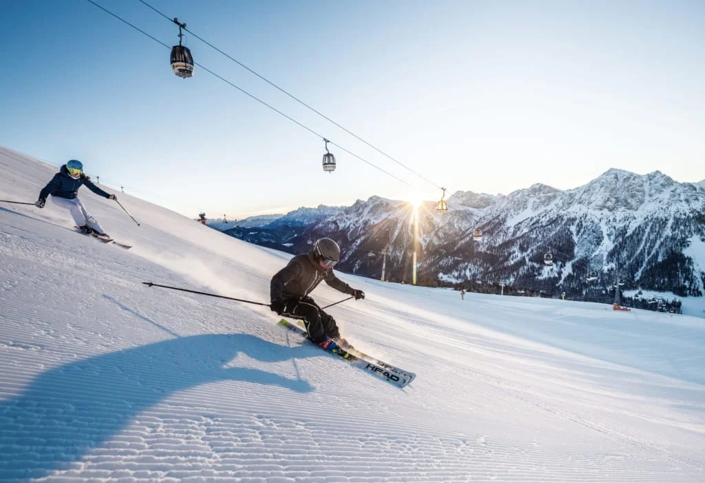 Two skiers skiing down a sunlit snowy mountain slope
