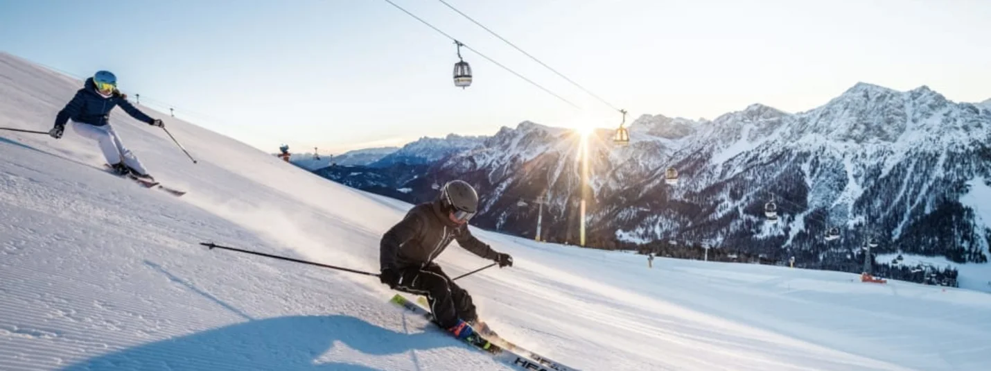 Dolomiti Super Première 4=3 Twee skiërs skiën op een besneeuwde berghelling in de zon