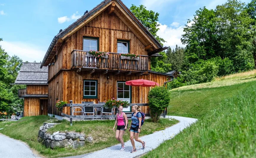 Wooden house in green landscape with two women hiking in front