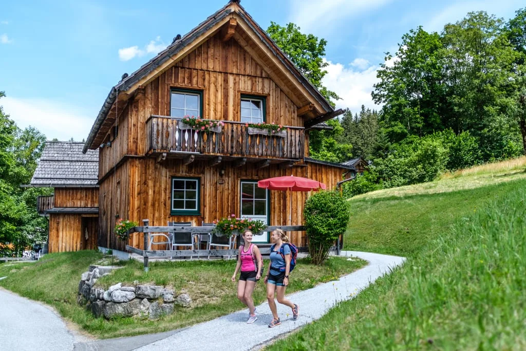 Houten huis in groen landschap met twee wandelende vrouwen ervoor
